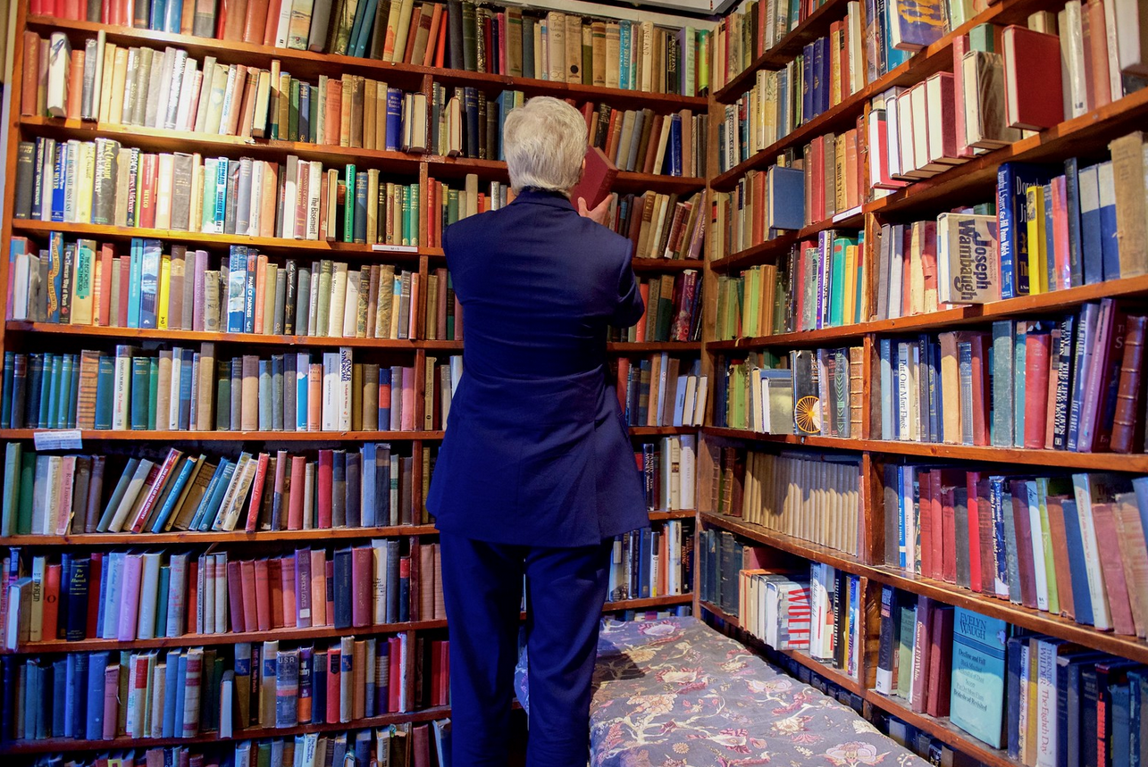 An older man lifts a book from a bookshelf in a library