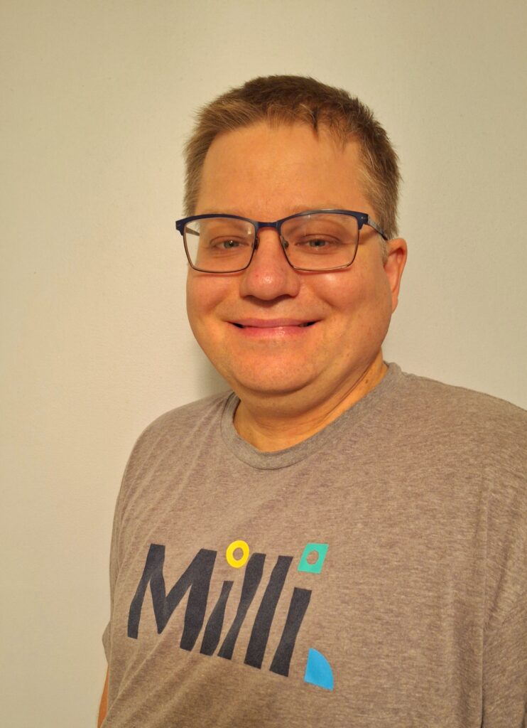 Photo of Matthew Cherne, smiling and wearing glasses and a grey t-shirt with the Milli logo on the front